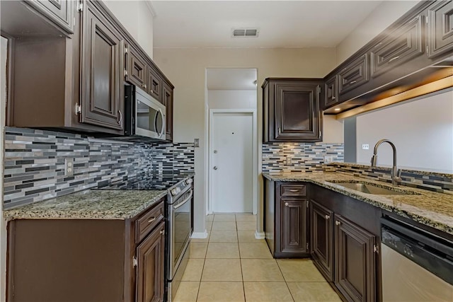 kitchen featuring light stone counters, dark brown cabinetry, stainless steel appliances, a sink, and visible vents