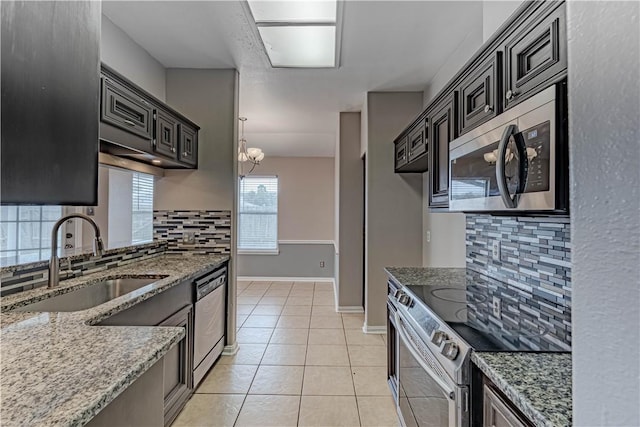 kitchen featuring light stone counters, light tile patterned flooring, dark cabinets, a sink, and appliances with stainless steel finishes