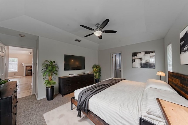 bedroom with light carpet, visible vents, a tray ceiling, vaulted ceiling, and a fireplace