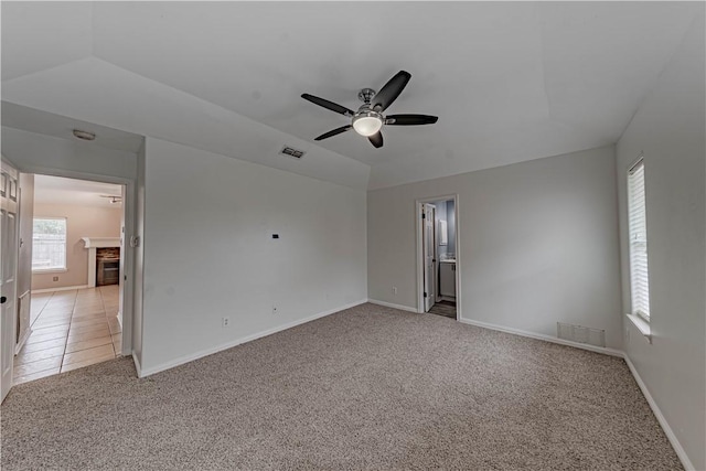 empty room featuring light carpet, baseboards, visible vents, and vaulted ceiling