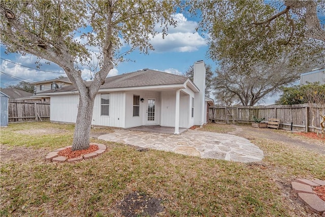 back of property with a fenced backyard, a chimney, a lawn, and a patio