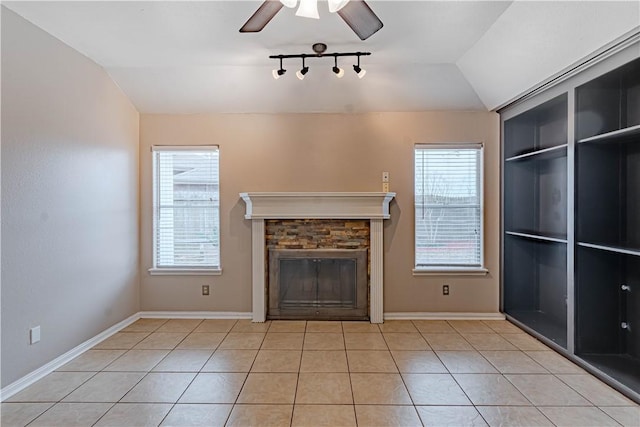 unfurnished living room with ceiling fan, vaulted ceiling, a stone fireplace, and light tile patterned floors