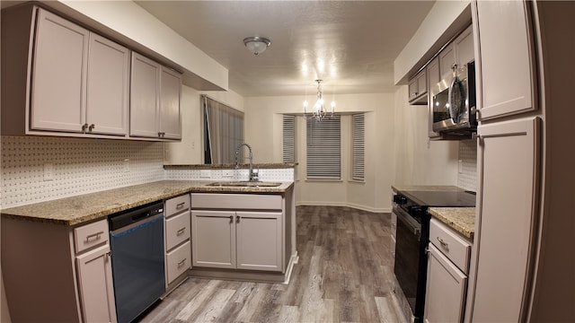 kitchen featuring kitchen peninsula, light stone countertops, sink, black appliances, and hardwood / wood-style flooring