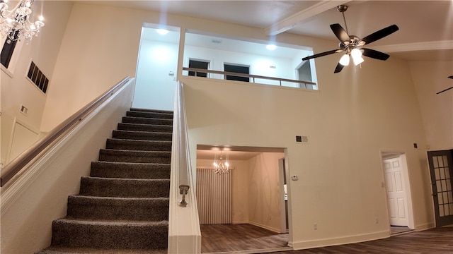 staircase with hardwood / wood-style flooring, ceiling fan with notable chandelier, a towering ceiling, and beamed ceiling