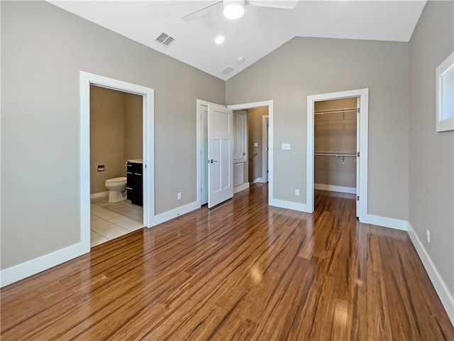 unfurnished bedroom featuring ensuite bath, vaulted ceiling, light hardwood / wood-style flooring, ceiling fan, and a spacious closet