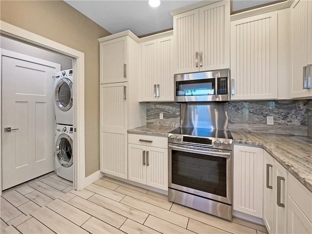 kitchen featuring stacked washing maching and dryer, backsplash, appliances with stainless steel finishes, light stone countertops, and light hardwood / wood-style flooring