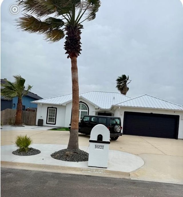 view of front of house featuring fence, concrete driveway, stucco siding, metal roof, and an attached garage