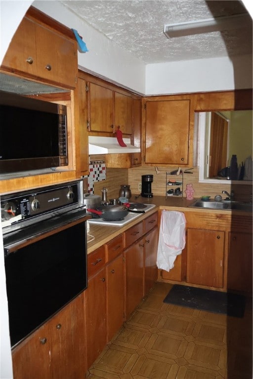 kitchen featuring sink, backsplash, oven, and a textured ceiling