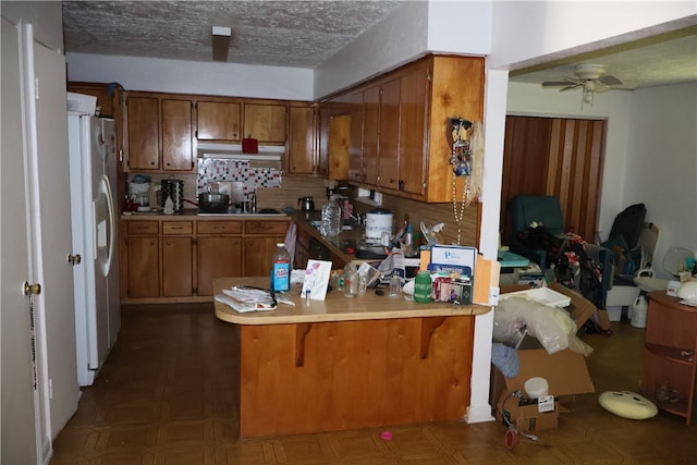 kitchen with kitchen peninsula, ceiling fan, a textured ceiling, white refrigerator with ice dispenser, and decorative backsplash