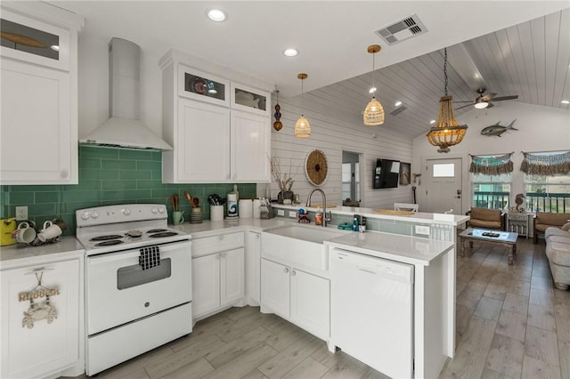 kitchen with decorative light fixtures, kitchen peninsula, white appliances, wall chimney range hood, and white cabinets