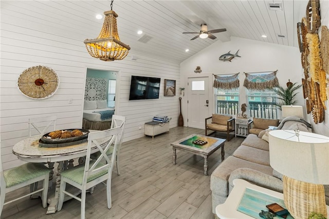 living room featuring light hardwood / wood-style flooring, high vaulted ceiling, ceiling fan with notable chandelier, wooden ceiling, and wood walls