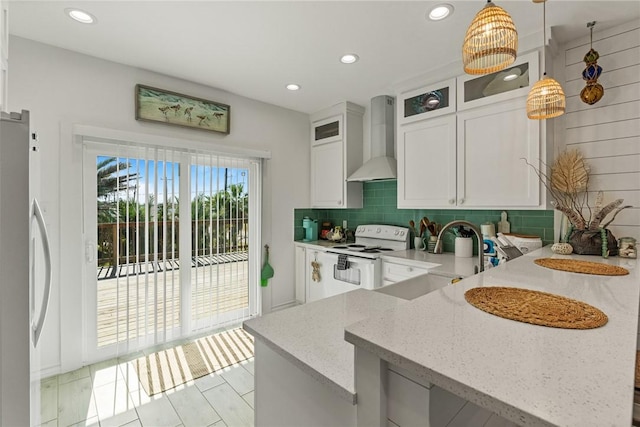 kitchen featuring wall chimney range hood, stainless steel refrigerator, white cabinetry, hanging light fixtures, and white electric stove