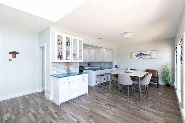 kitchen featuring glass insert cabinets, wood finished floors, a breakfast bar area, white cabinets, and decorative backsplash