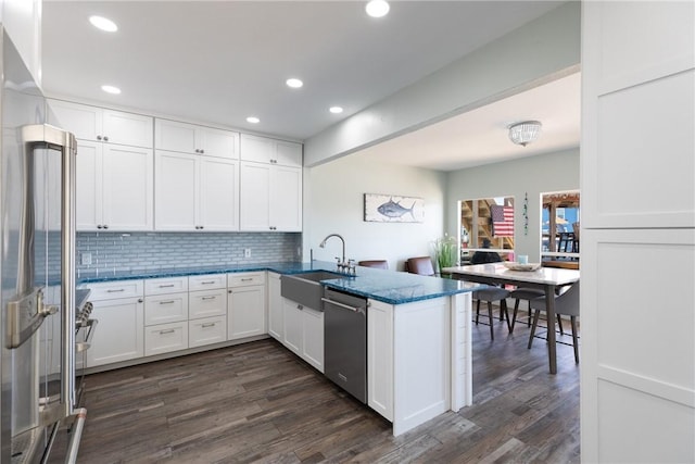 kitchen with a peninsula, a sink, white cabinets, appliances with stainless steel finishes, and backsplash