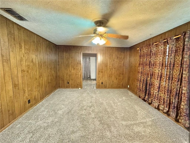 carpeted spare room featuring wooden walls and a textured ceiling