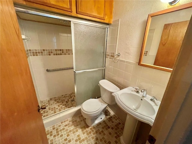 bathroom featuring sink, a shower with shower door, tile walls, toilet, and tile patterned floors