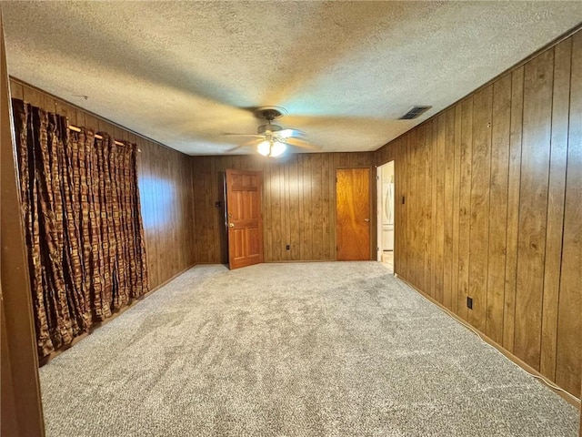 carpeted empty room with a textured ceiling, wood walls, and ceiling fan