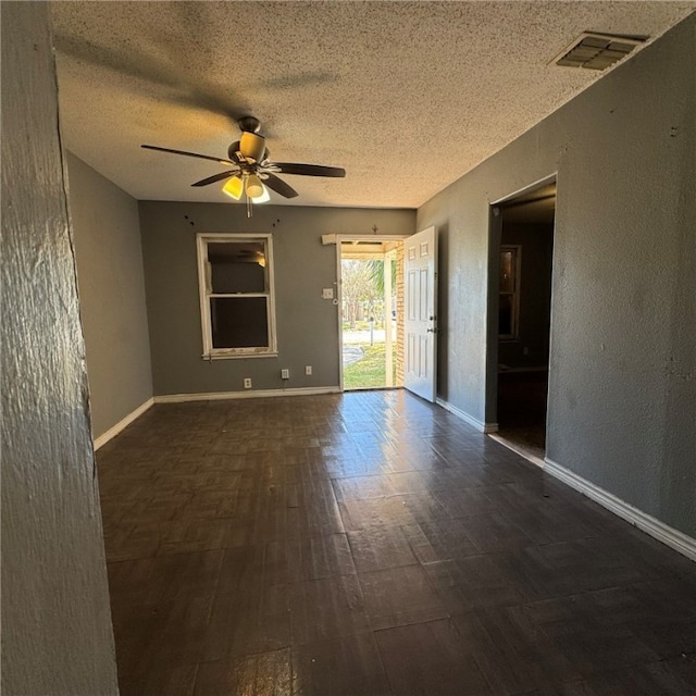 empty room featuring ceiling fan, dark wood-type flooring, and a textured ceiling