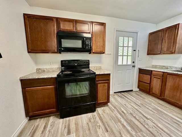 kitchen with light wood-type flooring, black appliances, and light stone countertops