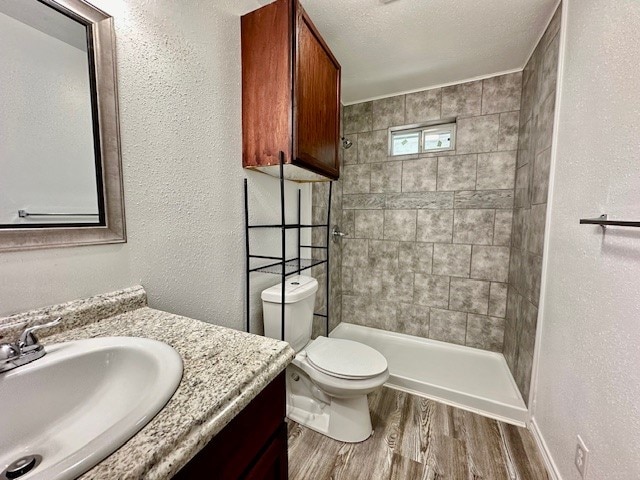 bathroom featuring a textured ceiling, hardwood / wood-style floors, vanity, tiled shower, and toilet