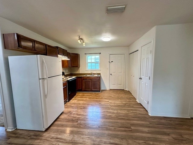 kitchen with white appliances, dark brown cabinets, sink, and light hardwood / wood-style flooring