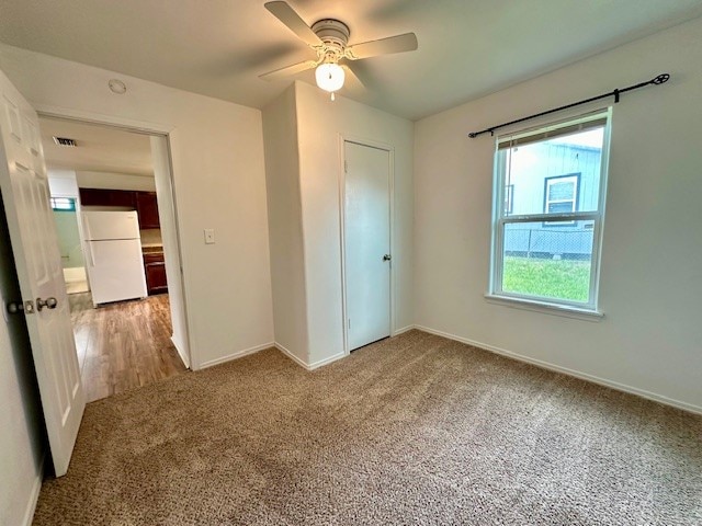 unfurnished bedroom featuring ceiling fan, a closet, white refrigerator, and carpet