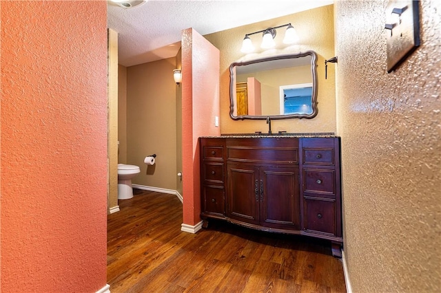 bathroom featuring wood-type flooring, toilet, vanity, and a textured ceiling