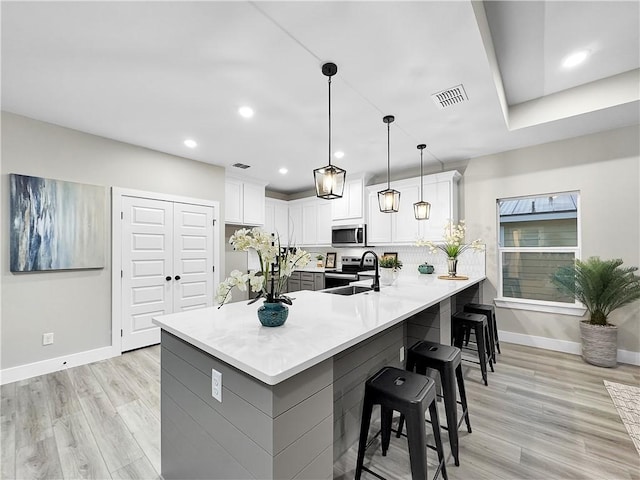 kitchen featuring sink, stainless steel appliances, white cabinets, decorative light fixtures, and kitchen peninsula