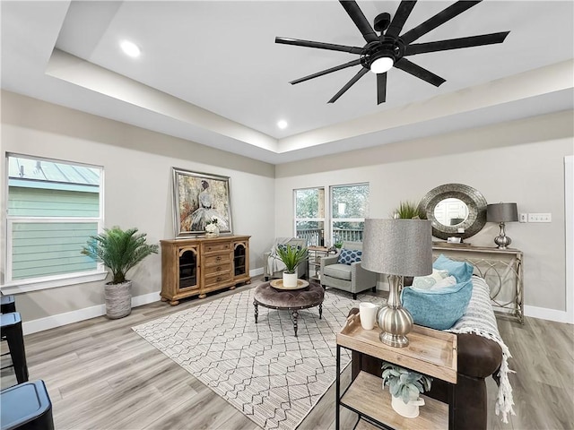 living room with ceiling fan, a tray ceiling, and light wood-type flooring