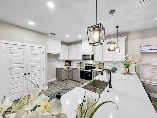 kitchen featuring decorative light fixtures, light wood-type flooring, appliances with stainless steel finishes, kitchen peninsula, and white cabinets