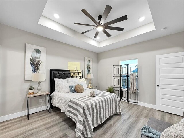 bedroom with hardwood / wood-style flooring, ceiling fan, and a tray ceiling