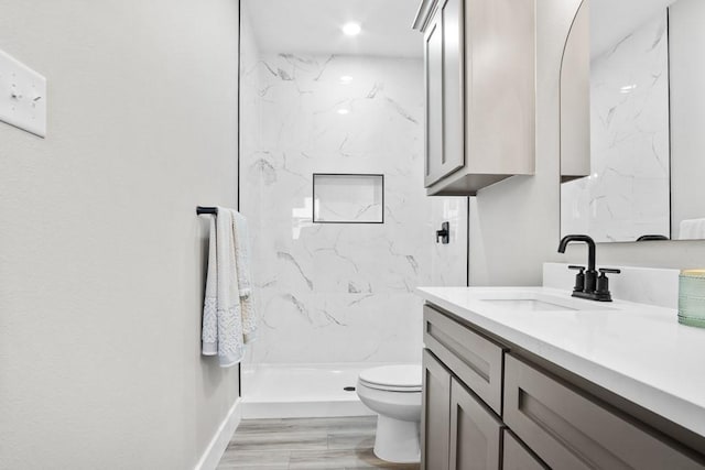 bathroom with hardwood / wood-style floors, vanity, a tile shower, and toilet