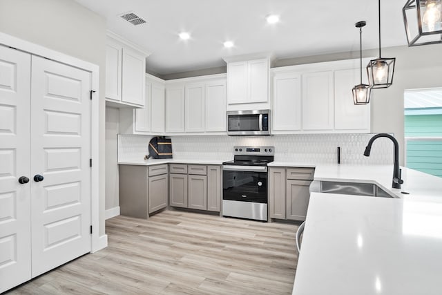 kitchen with sink, gray cabinetry, white cabinetry, hanging light fixtures, and appliances with stainless steel finishes