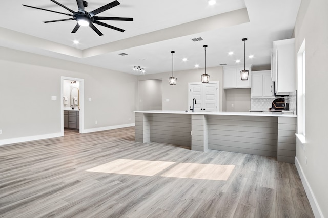 kitchen with hanging light fixtures, a tray ceiling, light hardwood / wood-style floors, white cabinets, and decorative backsplash