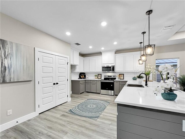 kitchen featuring sink, gray cabinetry, backsplash, hanging light fixtures, and stainless steel appliances