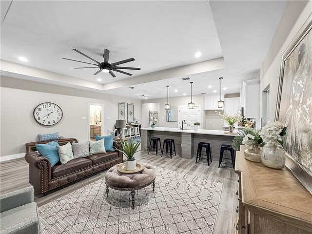 living room with a raised ceiling, ceiling fan, sink, and light hardwood / wood-style floors