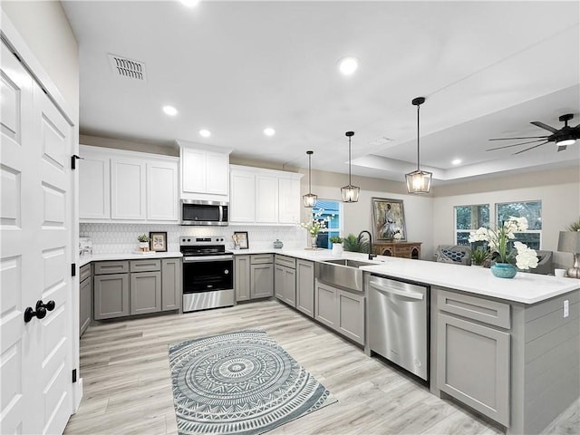 kitchen featuring sink, hanging light fixtures, gray cabinets, kitchen peninsula, and stainless steel appliances