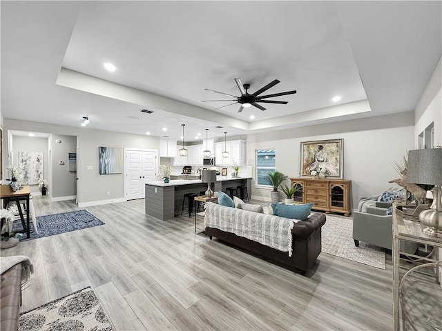 living room featuring a tray ceiling, ceiling fan, and light wood-type flooring