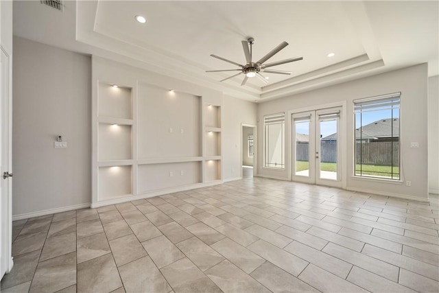 empty room featuring baseboards, a raised ceiling, built in shelves, and a ceiling fan