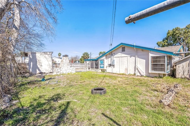 view of yard featuring a fire pit, a storage shed, fence, and an outbuilding