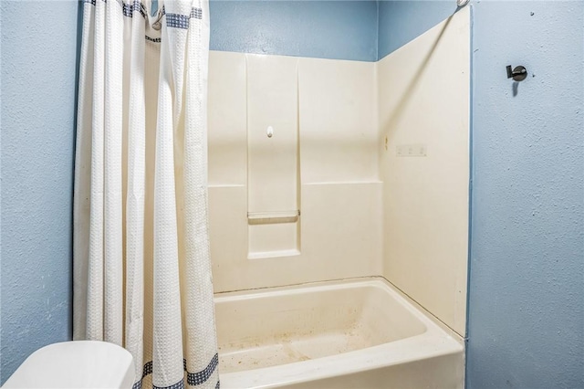 full bathroom with a textured wall, shower / bath combo with shower curtain, and toilet