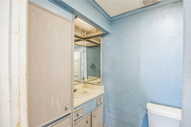 half bath featuring visible vents, a textured wall, vanity, and toilet