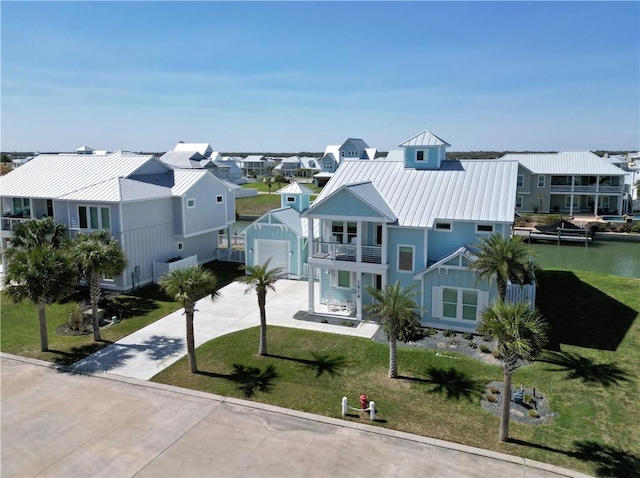 view of front of house with a balcony, concrete driveway, a residential view, a front lawn, and a standing seam roof