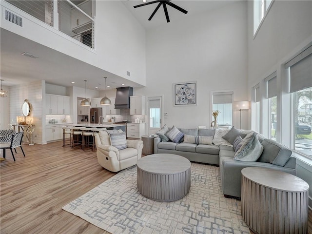 living room featuring ceiling fan with notable chandelier, visible vents, and light wood-style floors