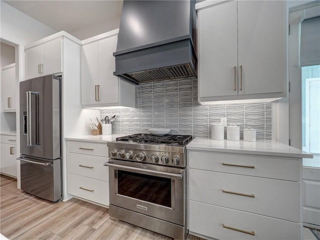 kitchen with light wood-style flooring, high quality appliances, light countertops, custom exhaust hood, and tasteful backsplash