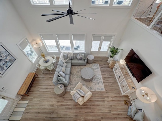 living area with a ceiling fan, baseboards, a high ceiling, and wood finished floors