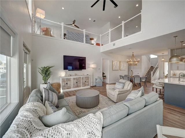 living area with recessed lighting, ceiling fan with notable chandelier, wood finished floors, a towering ceiling, and visible vents