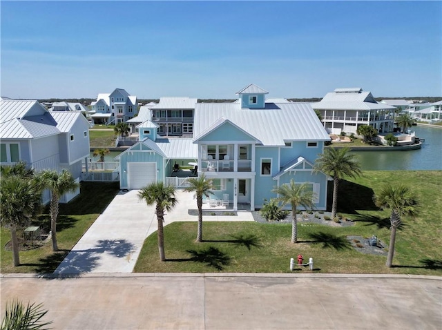 view of front of home with driveway, a standing seam roof, a front yard, and a balcony