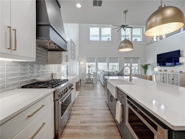 kitchen with custom range hood, open floor plan, backsplash, high end stainless steel range, and a sink