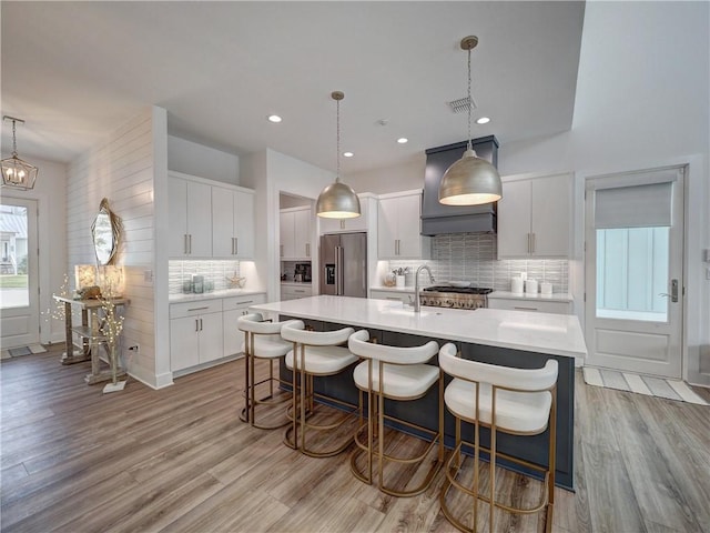 kitchen featuring light countertops, high quality fridge, light wood finished floors, and an island with sink